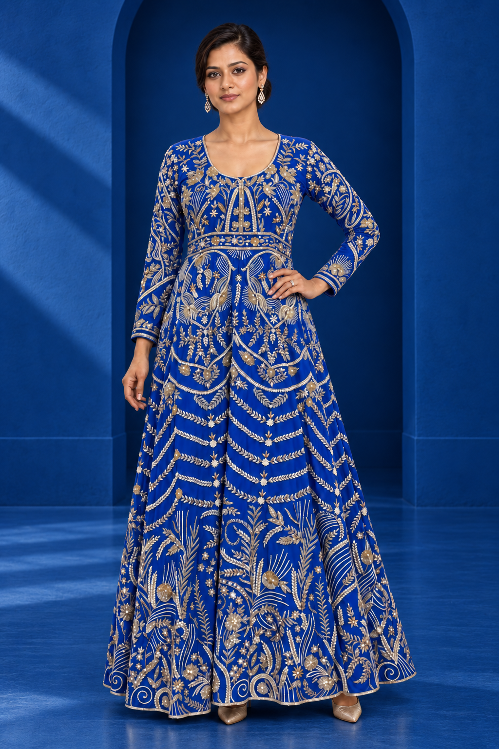 Royal blue floor-length anarkali with pale-gold floral embroidery, shown in a blue architectural setting